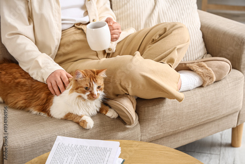 Foto Woman in beige slippers with coffee cup and cute cat on sofa at home