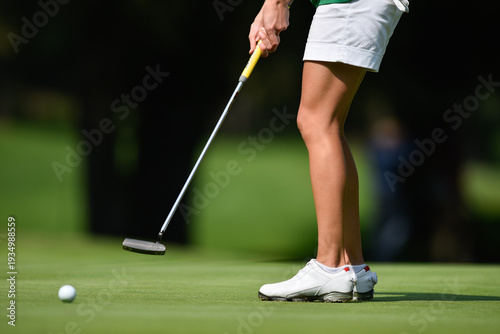 A golfer prepares to putt on a green under bright sunlight.