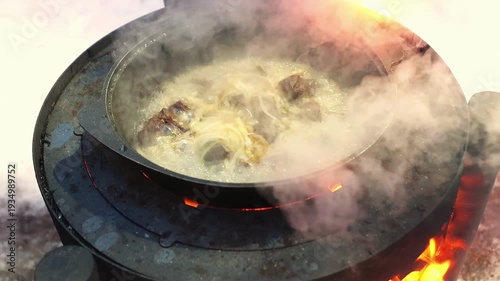 Traditional outdoor stove used for pilaf cooking in winter conditions. Rustic fire cooking, camping lifestyle and cozy seasonal atmosphere. Rice with beef meat boiling and steaming.