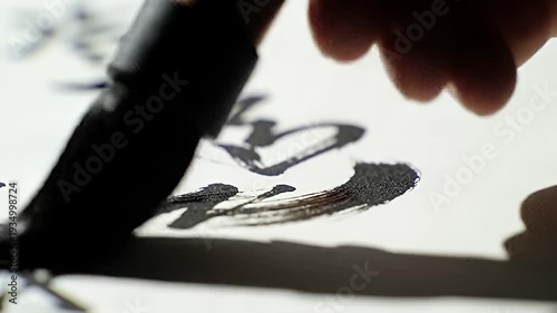 A calligraphy brush writes Asian characters on paper using black ink, close-up detail