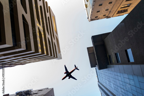 Canvas Print Airplane flying low over business skyscrapers building on blue sky