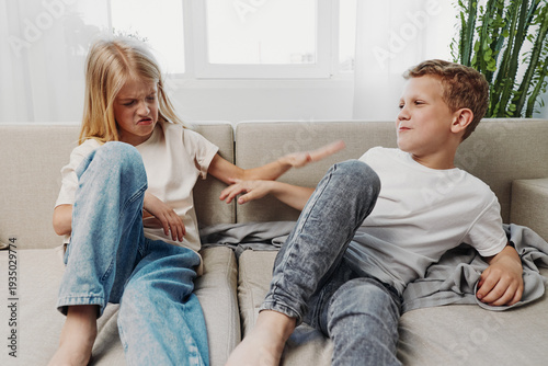 Slika na platnu Two children sitting on a couch, a boy and a girl arguing with frustrated and annoyed expressions in a bright living room setting