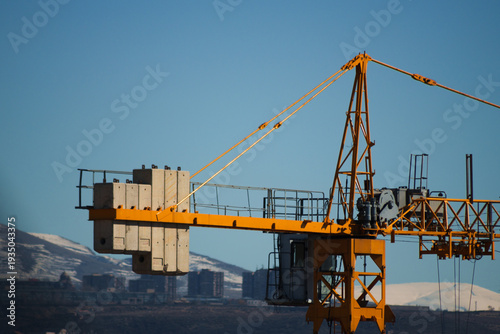 Foto Yellow tower crane against the backdrop of the city from a close distance, The rear part of the tower crane is a console or counter-jib, reinforced concrete or metal counterweight slabs