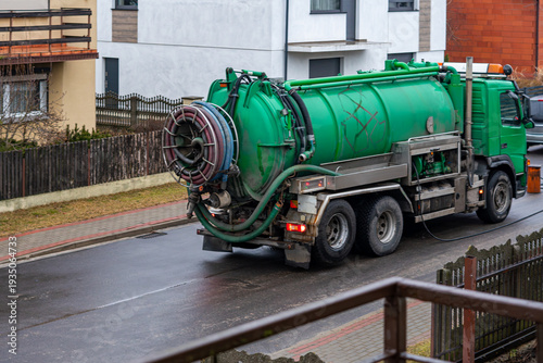 Green vacuum truck, sewage suction truck for septic tank emptying on residential street, professional municipal service vehicle and high-pressure sewer cleaning equipment in urban environment.