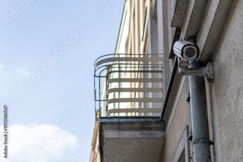 Outdoor CCTV security camera mounted on a building facade, professional surveillance system near a rain pipe, property protection and video monitoring against blue sky, close-up of urban security equi