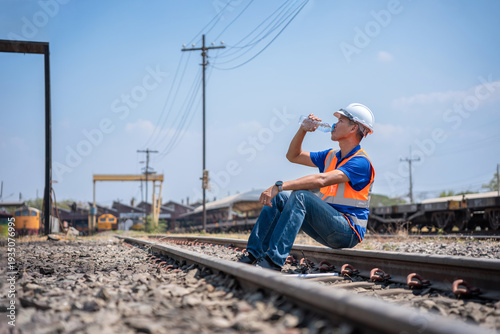 Photos Railway worker sitting on tracks drinking water to stay hydrated under hot sun,