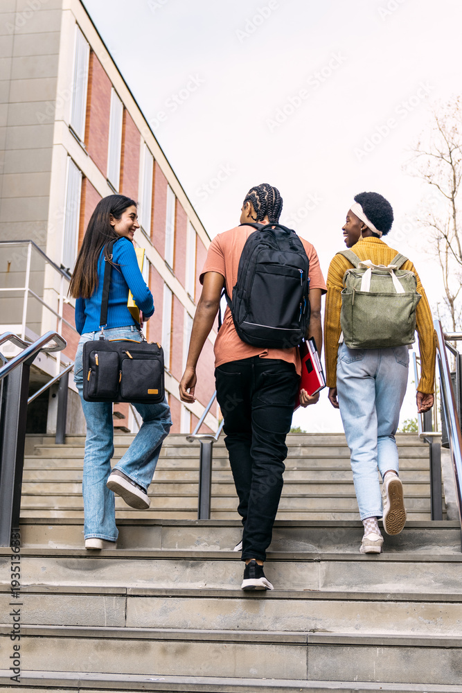 Obraz premium Diverse group of young students walking down university stairs, carrying backpacks and books while engaging in conversation