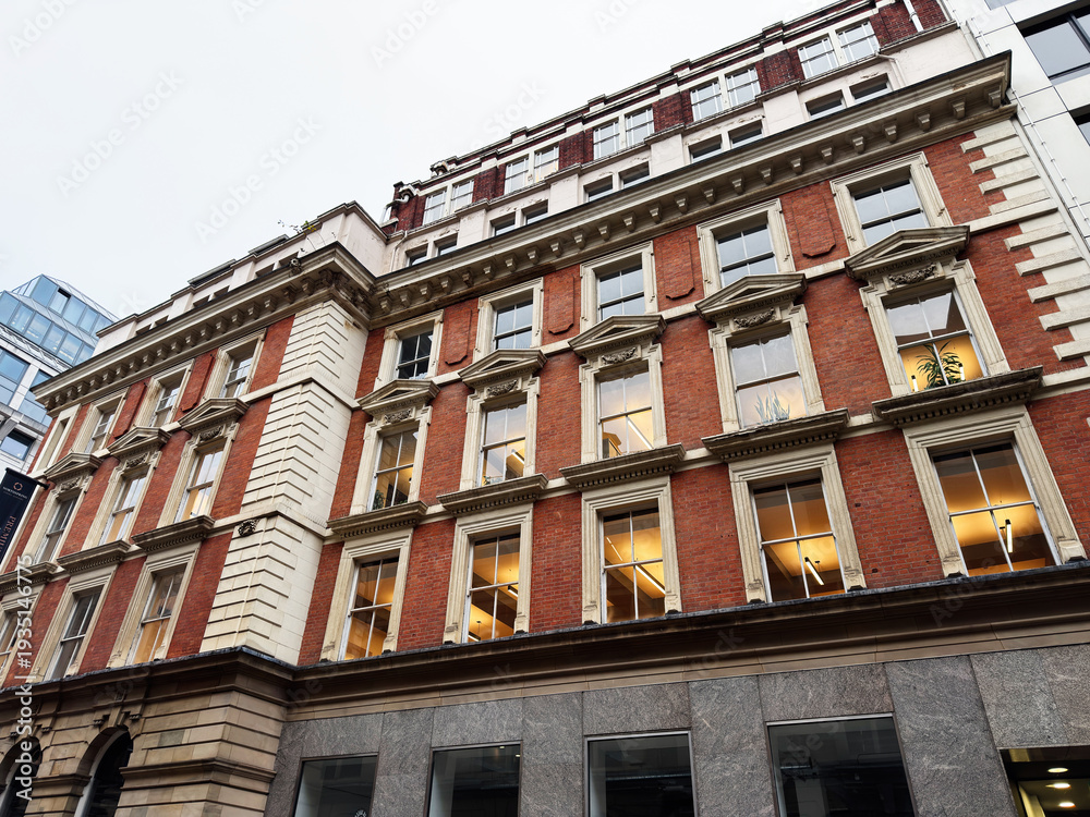 Naklejka premium Historic red brick building with ornate windows along a city street in Manchester UK