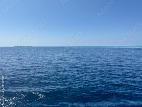Bild auf Leinwand Beautiful deep blue sea water surface with a small distant island on the horizon under a clear sky