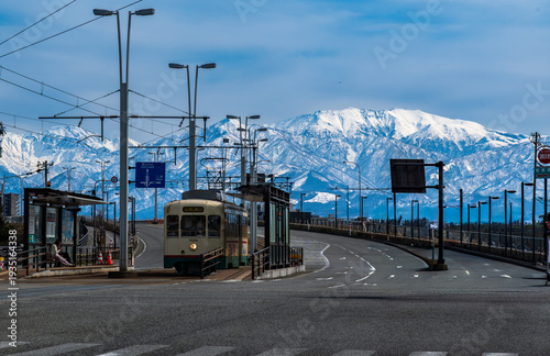 雪の立山連峰を背景に富山市呉羽橋を渡る路面電車