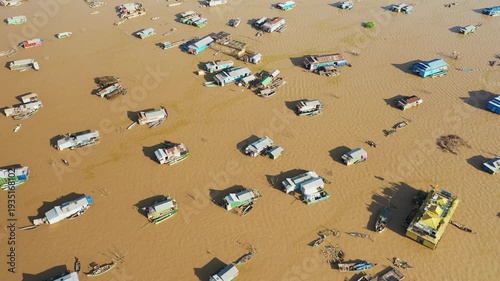 Aerial view of the floating village of Chong Kneas on Tonle Sap Lake, Cambodia, featuring scattered houseboats and muddy water. Unique rural lifestyle and traditional architecture are visible from