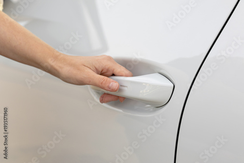 Hand reaching for white car door handle, showcasing modern vehicle design and sleek exterior, emphasizing accessibility and user-friendly features in automotive context