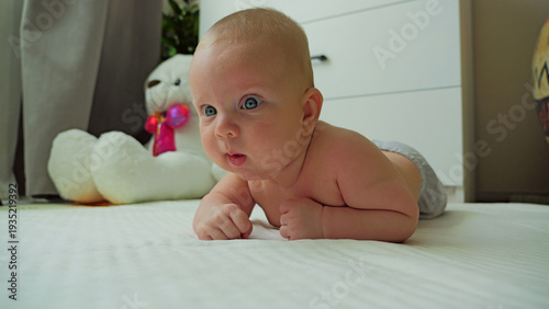 Valokuva A curious blue-eyed infant practices tummy time on a soft white mat