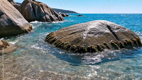 Clear blue ocean water gently washes over large sunlit s on a beautiful day.