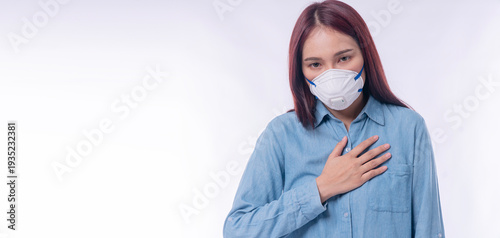 Young Asian woman wearing N95 face mask holding her chest with breathing difficulty. Sick female patient with copy space for air pollution, PM 2.5, and virus protection concept.