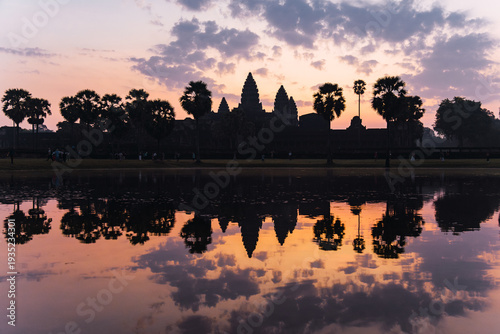 Angkor wat temple complex and palm trees reflecting in water at dawn