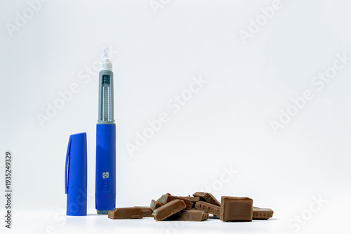Bilde på lerret Blue insulin injector pen like ozempic standing next to milk chocolate pieces is