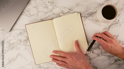 Organized workspace featuring a laptop, black notebook, pen, and coffee on a white marble desk. This clean setup is ideal for writing, studying, or focused work sessions at home or office