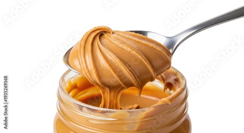 A spoon scoops creamy peanut butter from a glass jar on a white background