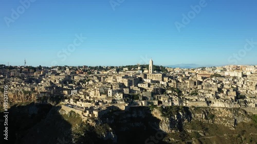 Wide aerial panorama of Matera, Italy, showcasing ancient stone buildings and dramatic cliffs under a clear blue sky.