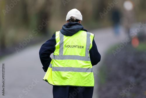 Принти на полотні A volunteer viewed from behind wearing a bright yellow high-vis vest marked VOL