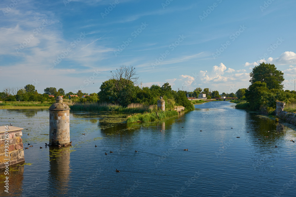Obraz premium Wide view of the historic Stone Lock (Kamienna Sluza) and the Motlawa River with ducks under a blue sky, Gdansk, Pomerania, Poland, Europe.