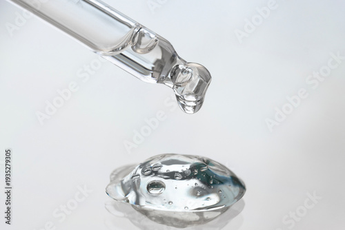 One pipette filled with hyaluronic acid with a drop on a neutral background, macro view from the front.