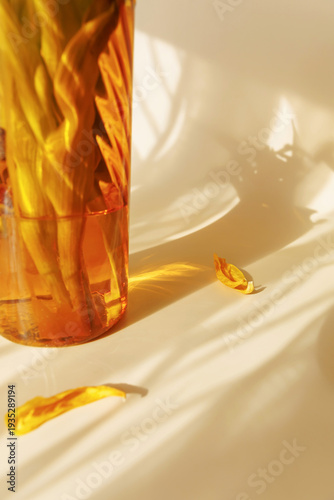 Photography Close up of amber glass vase with wilted yellow iris petals and warm sunlight re