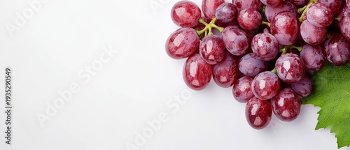 Fresh red grapes with lush green leaves set against a clean, white background