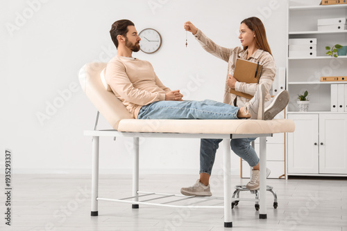 Tablou pe pânză Female psychologist with pendulum hypnotizing young man on couch in office