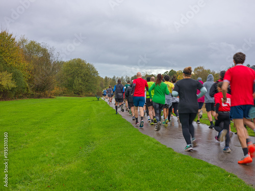 Foto A large group of runners viewed from behind running along a glistening wet tarma