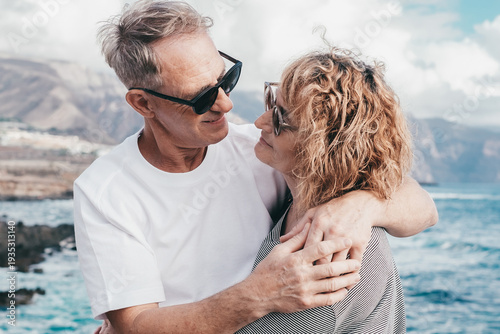 Lovely mature and romantic senior couple embrace each other on the seashore looking into each other's eyes, two embraced people stay together expressing love and tenderness