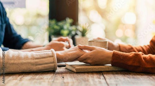 Tableau sur toile Two people holding hands across a wooden table, symbolizing connection, comfort, and support in a warm environment