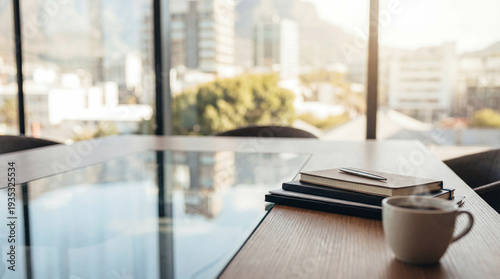 Obraz na płótnie A sophisticated office meeting table with a reflective glass top, featuring a stack of notebooks, a pen, and a ceramic cup of coffee near the edge, with a city view through large windows