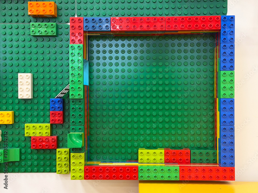 Fototapeta premium Colorful toy brick square frame on green baseplate