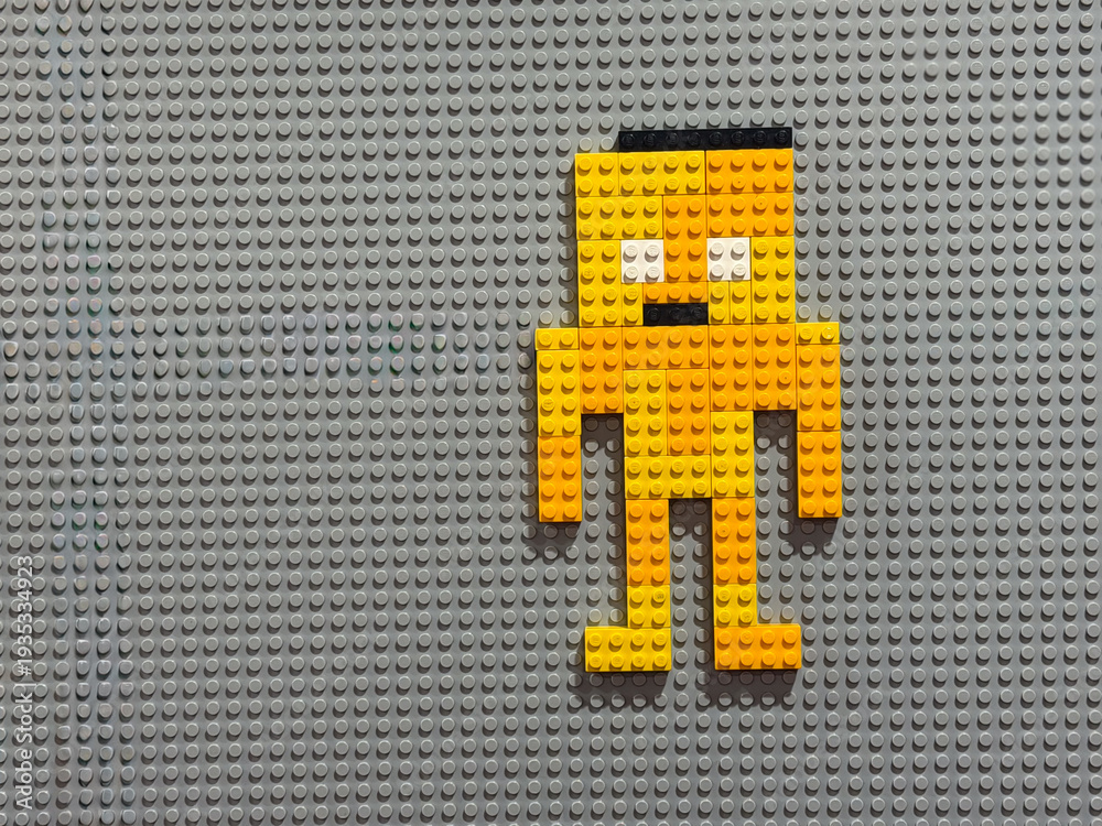 Fototapeta premium Yellow brick pixel-robot on gray baseplate