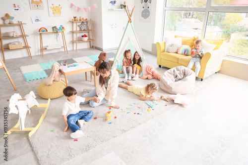 Cute little children with nursery teacher playing in kindergarten