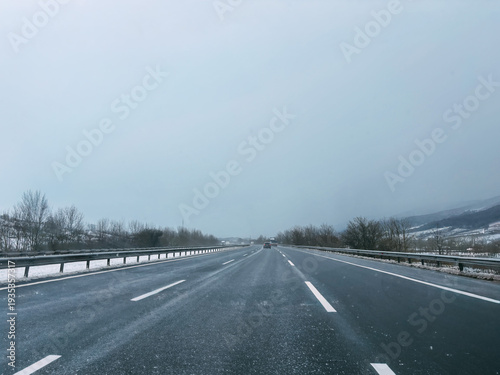 Driving on a wet highway in winter with light snow and grey sky