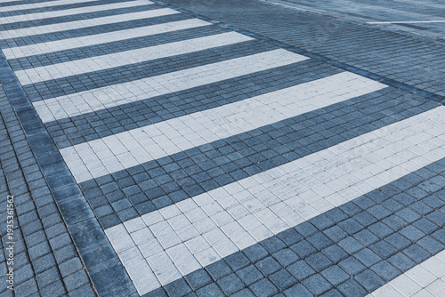 Pedestrian crossing markings creating a rhythmic pattern of white and blue stripes on a textured paved street surface