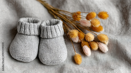 Soft gray baby booties beside dried flowers on textured background  