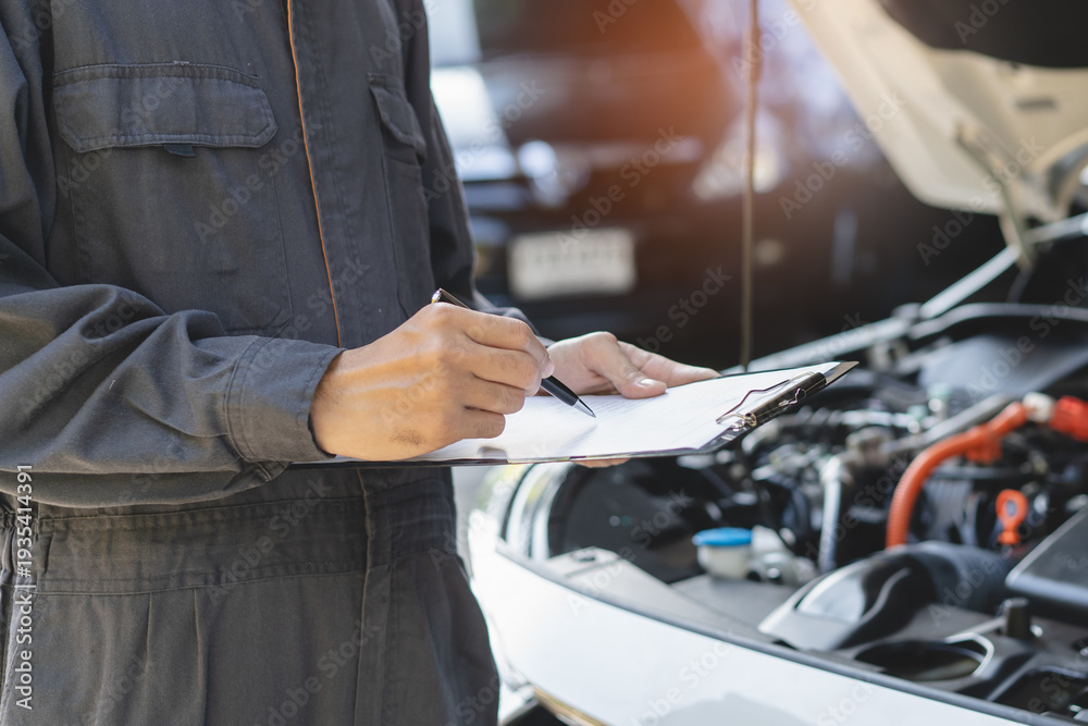 Obraz premium Auto check up and car service shop concept. Mechanic writing job checklist to clipboard to estimate repair quotation to client at workshop garage.