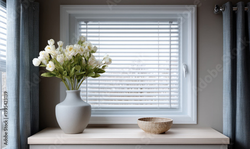 White tulip flower arrangement in ceramic vase beside woven basket on wooden table, modern kitchen window with blinds, soft natural light
