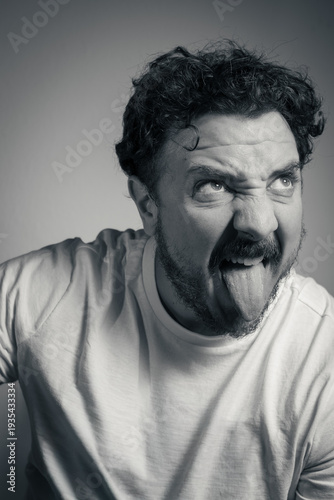 Funny man sticking out tongue with crossed eyes and silly expression black and white portrait
