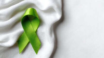 Green awareness ribbon on white silk fabric for mental health awareness campaign, charity support, Donate Life Month