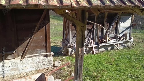 Old rusty wheelbarrow beside rustic farm building with clay tile roof in rural countryside