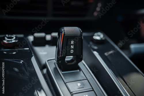 A compact knurled gear selector with R N D and an illuminated P button sits on a glossy black center console in a Porsche 911 Carrera, indoors with moody lighting.