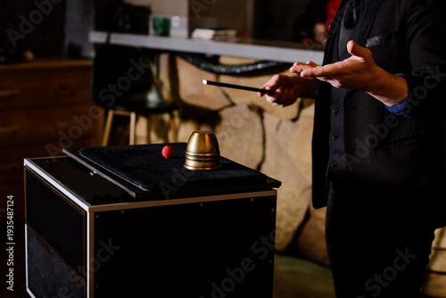 Close-up of a professional magician in a black suit performing a classic cup and ball trick with a magic wand at a corporate event or party.