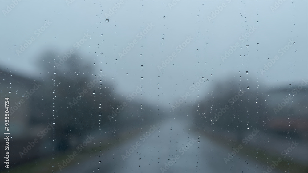 Obraz premium Raindrops Sliding Down a Car Windshield with Blurred Street View during Heavy Rainfall Creating Moody Atmospheric Effect for Travel or Weather Themed Visuals