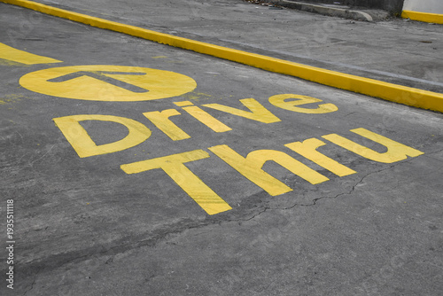 Yellow Drive Thru sign painted on a cemented road to guide customers where to go to order. Clean road and clear sign.