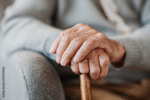 Worn hands grip a wooden cane for support. Soft knit sleeves frame the gentle grip. Calm posture suggests quiet comfort. Elderly hands convey wisdom and resilience. Ideal for stories of aging, dignity